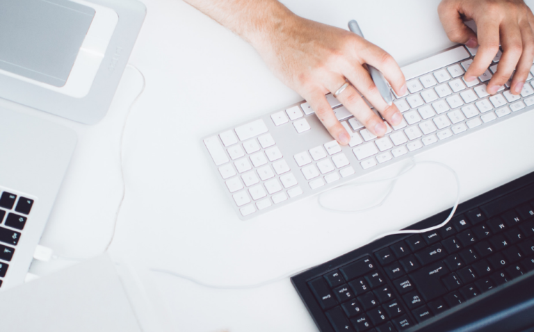 A person holding a pen facing computer while typing on a keyboard demonstrating working with your assistant remotely.