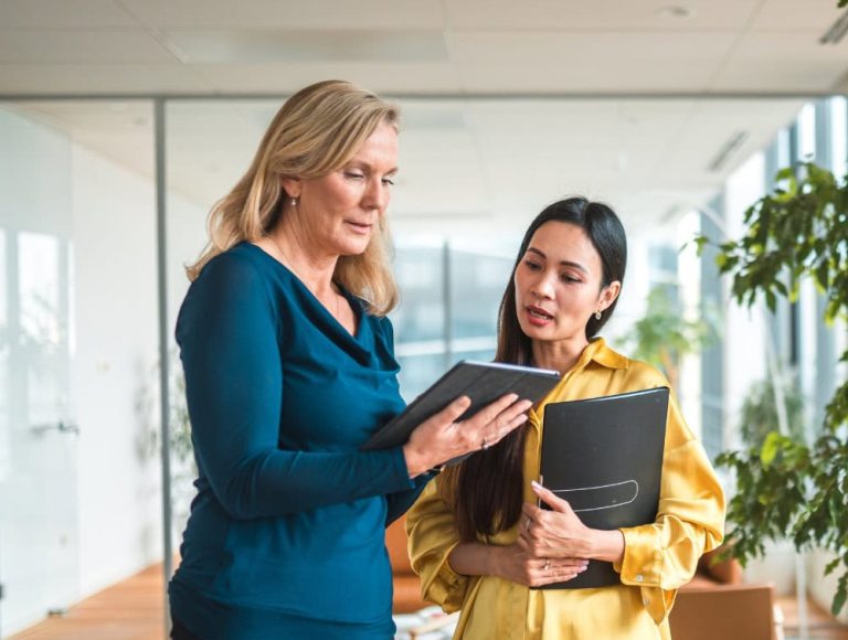 Executive providing guidance to assistant with tablet and documents, illustrating how to prevent why delegation fails.