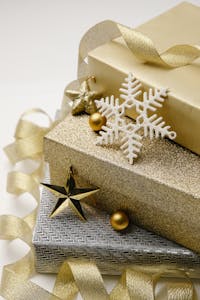 Christmas composition of stack of gift boxes wrapped in silver and golden paper cute baubles and wavy ribbon