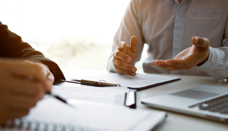 Two people at an office desk are discussing and taking notes during a giving effective feedback conversation.