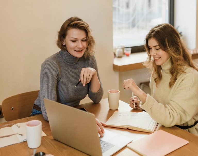 Two women engaged in a training, at a coffee shop using a laptop.