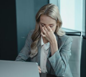 Businesswoman showing stress at her desk with a laptop, highlighting work pressure.