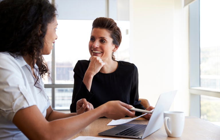Two women in an office having an executive assistant mid-year check-in meeting.